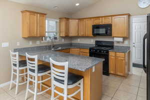 Kitchen featuring black appliances, a breakfast bar, dark stone counters, and vaulted ceiling