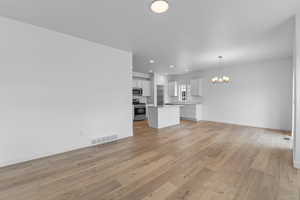 Unfurnished living room featuring an inviting chandelier and light hardwood / wood-style floors