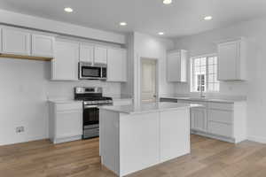 Kitchen featuring light wood-type flooring, stainless steel appliances, white cabinetry, sink, and a kitchen island