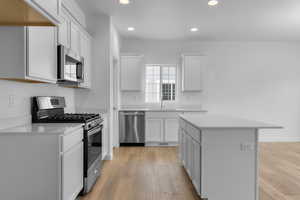 Kitchen featuring light wood-type flooring, stainless steel appliances, a center island, sink, and white cabinets