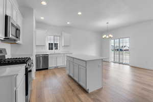 Kitchen featuring appliances with stainless steel finishes, a center island, sink, light wood-type flooring, and white cabinets