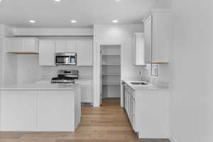 Kitchen with appliances with stainless steel finishes, light hardwood / wood-style floors, white cabinetry, and sink