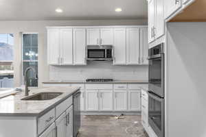 Kitchen featuring light stone countertops, appliances with stainless steel finishes, dark hardwood / wood-style flooring, sink, and white cabinets