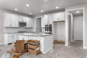 Kitchen featuring cooktop, sink, white cabinetry, and an island with sink