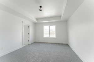 Carpeted empty room with a textured ceiling, baseboards, and a raised ceiling