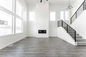 Unfurnished living room with stairs, a towering ceiling, wood finished floors, a chandelier, and baseboards