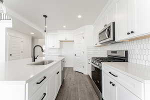 Kitchen with stainless steel appliances, a sink, wood finished floors, decorative backsplash, and recessed lighting