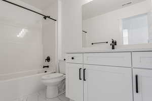 Full bathroom with marble look tiles, toilet, vanity, and shower / bath combination
