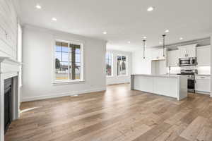 Kitchen featuring white cabinetry, decorative light fixtures, stainless steel appliances, a center island with sink, and light hardwood / wood-style floors