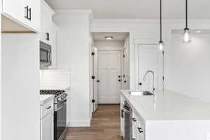 Kitchen featuring light hardwood / wood-style flooring, backsplash, stainless steel appliances, sink, and white cabinetry