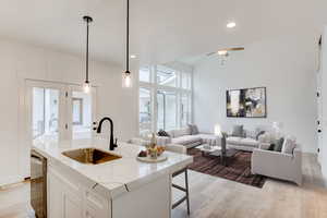 Kitchen featuring a kitchen island with sink, decorative light fixtures, sink, white cabinets, and light hardwood / wood-style floors