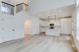 Kitchen featuring light wood-type flooring, white cabinetry, backsplash, stainless steel appliances, and a center island with sink