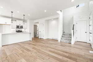 Unfurnished living room with ornamental molding, sink, and light hardwood / wood-style flooring