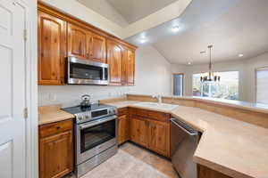 Kitchen featuring appliances with stainless steel finishes, sink, kitchen peninsula, a notable chandelier, and vaulted ceiling