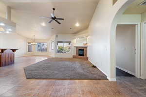 Unfurnished living room featuring vaulted ceiling, tile patterned flooring, ceiling fan with notable chandelier, and a tile fireplace