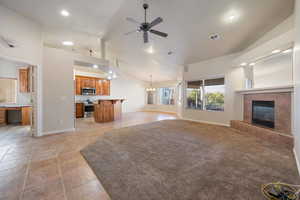 Living room with vaulted ceiling, light tile patterned flooring, ceiling fan with notable chandelier, and a tile fireplace