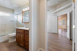 Full bathroom with hardwood / wood-style floors, shower / bath combination with glass door, vanity, and toilet