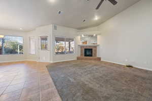 Unfurnished living room with vaulted ceiling, ceiling fan, a healthy amount of sunlight, and a fireplace