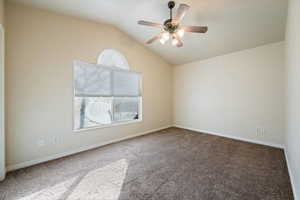 Carpeted empty room featuring ceiling fan and vaulted ceiling