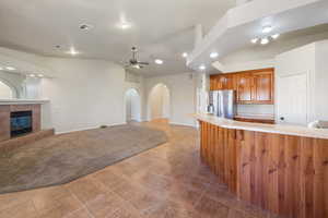 Kitchen featuring kitchen peninsula, stainless steel refrigerator with ice dispenser, ceiling fan, a fireplace, and vaulted ceiling