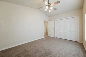 Unfurnished bedroom featuring ceiling fan, carpet, a closet, and vaulted ceiling