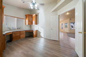 Home office with built in desk, ceiling fan, vaulted ceiling, and light hardwood / wood-style flooring