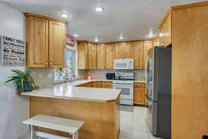 Kitchen with white appliances, sink, kitchen peninsula, and light tile patterned flooring