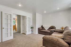 Carpeted living room with ornamental molding and french doors