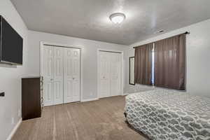 Bedroom featuring a textured ceiling, light colored carpet, and multiple closets