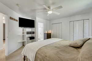 Bedroom with light colored carpet, connected bathroom, two closets, and ceiling fan