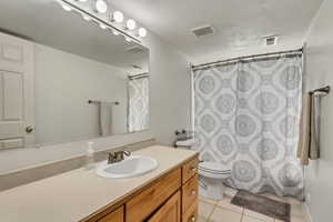 Bathroom with vanity, toilet, curtained shower, and tile patterned floors