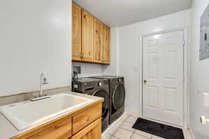 Clothes washing area with light tile patterned floors, cabinets, sink, and independent washer and dryer