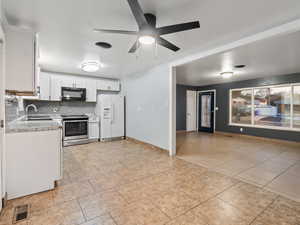 Kitchen with stainless steel electric range, white refrigerator with ice dispenser, backsplash, sink, and white cabinetry