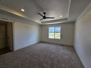 Empty room featuring carpet flooring, ceiling fan, a raised ceiling, and a textured ceiling