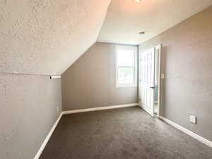 Bonus room featuring lofted ceiling, carpet, and a textured ceiling