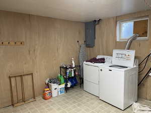 Laundry room featuring electric panel, a textured ceiling, wooden walls, and washing machine and clothes dryer