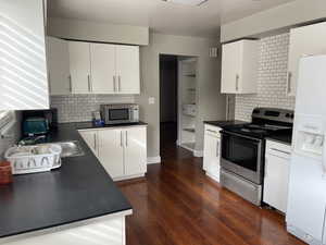 Kitchen featuring appliances with stainless steel finishes, white cabinetry, decorative backsplash, and dark hardwood / wood-style floors