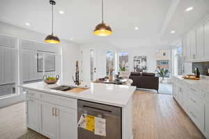 Kitchen with decorative light fixtures, white cabinetry, a center island with sink, and sink