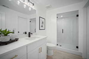 Bathroom featuring a textured ceiling, vanity, toilet, and walk in shower