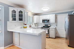 Kitchen featuring white cabinets, light wood-type flooring, stainless steel appliances, sink, and kitchen peninsula