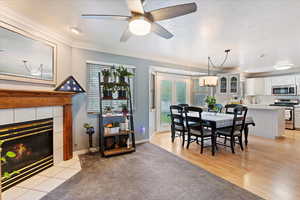 Dining room with a tiled fireplace, french doors, light wood-type flooring, ceiling fan, and ornamental molding