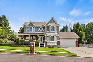 Victorian house featuring a garage, covered porch, and a front yard