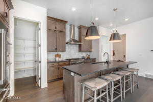 Kitchen featuring sink, wall chimney range hood, dark wood-type flooring, pendant lighting, and a breakfast bar