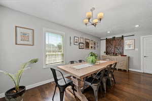 Dining space with a barn door, an inviting chandelier, dark hardwood / wood-style flooring, and a textured ceiling