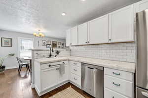 Kitchen with stainless steel appliances, sink, backsplash, and white cabinetry