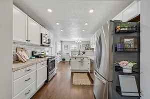 Kitchen featuring a textured ceiling, dark wood-type flooring, appliances with stainless steel finishes, and white cabinets