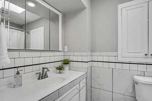 Bathroom with curtained shower, a skylight, backsplash, toilet, and vanity