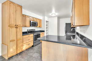 Kitchen with sink, appliances with stainless steel finishes, kitchen peninsula, and dark stone countertops