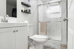 Bathroom featuring an enclosed shower, hardwood / wood-style flooring, toilet, washer / clothes dryer, and vanity