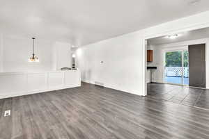 Unfurnished living room featuring dark wood-type flooring and a notable chandelier